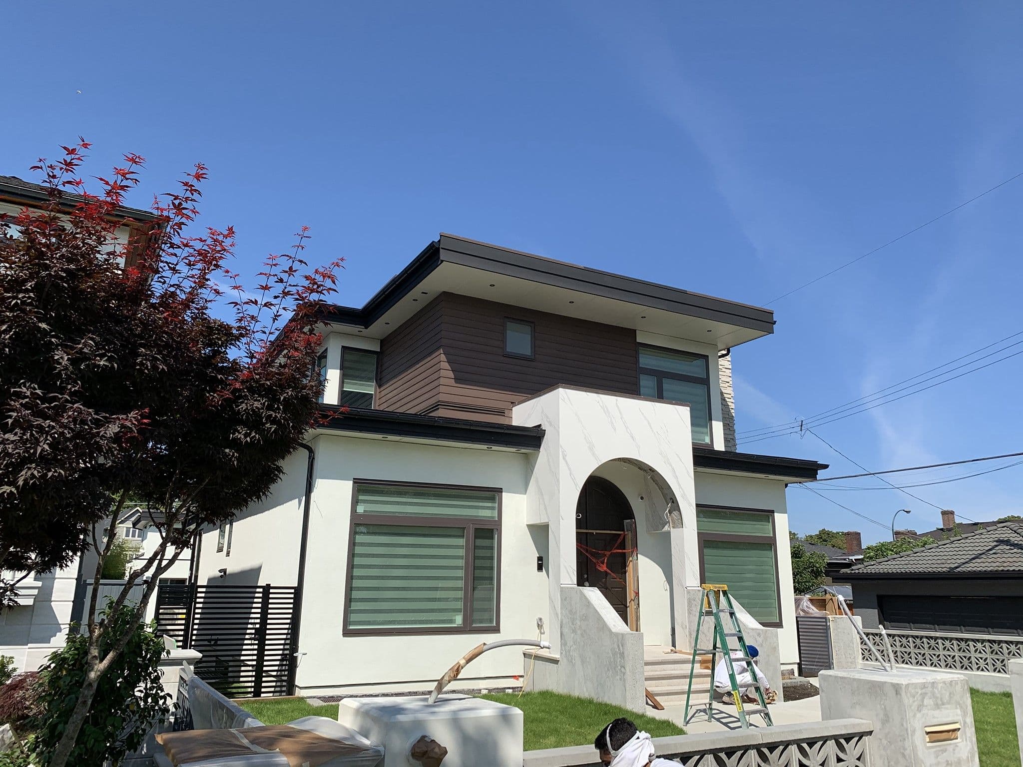 Modern two-storey home under construction with open garage and a large box-bay window; worker crouches amid building materials in the foreground.