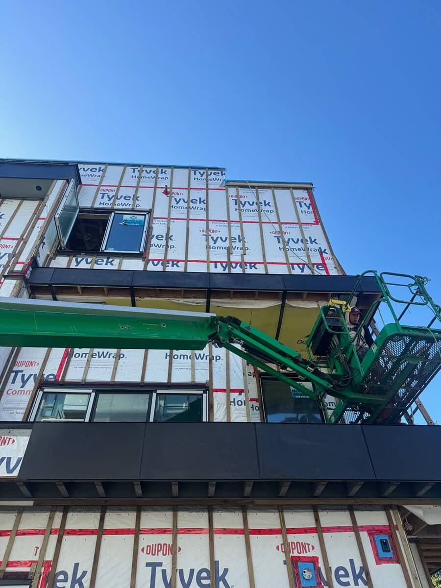 Modern mid-rise apartment building under construction with Tyvek panels and a crane suspended from the side.