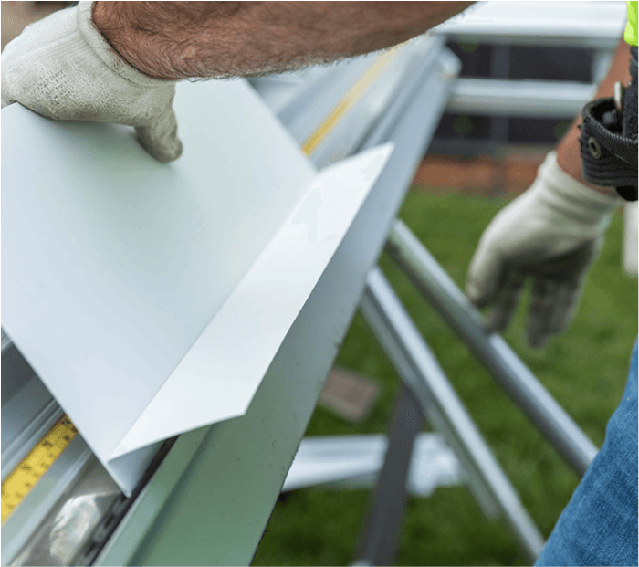 Construction worker shaping a piece of white metal flashing with gloves and tool